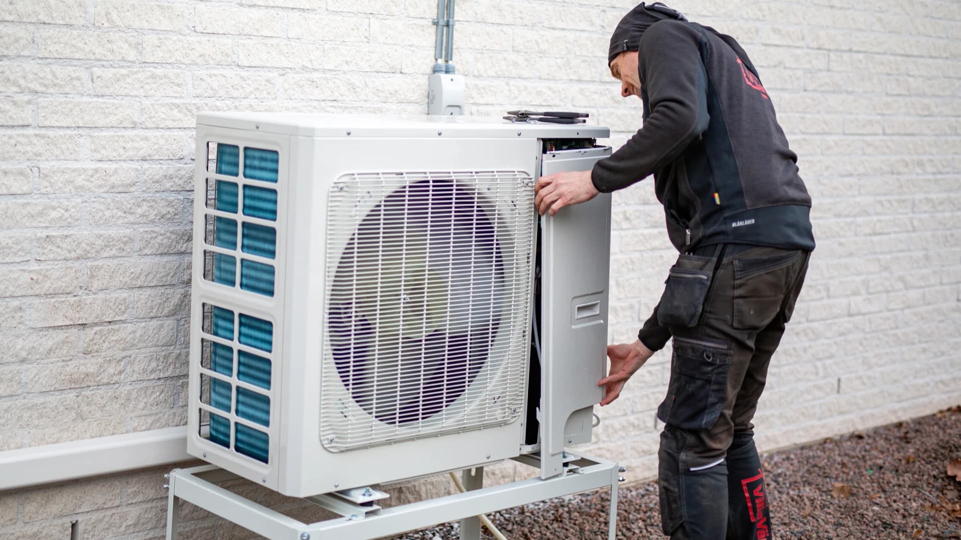 Installatör monterar värmepump på husvägg